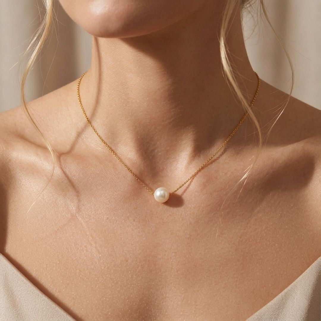 A delicate golden color sterling silver chain necklace with a single white 8-9mm pearl pendant, shown worn on a model's neck against a warm beige background.